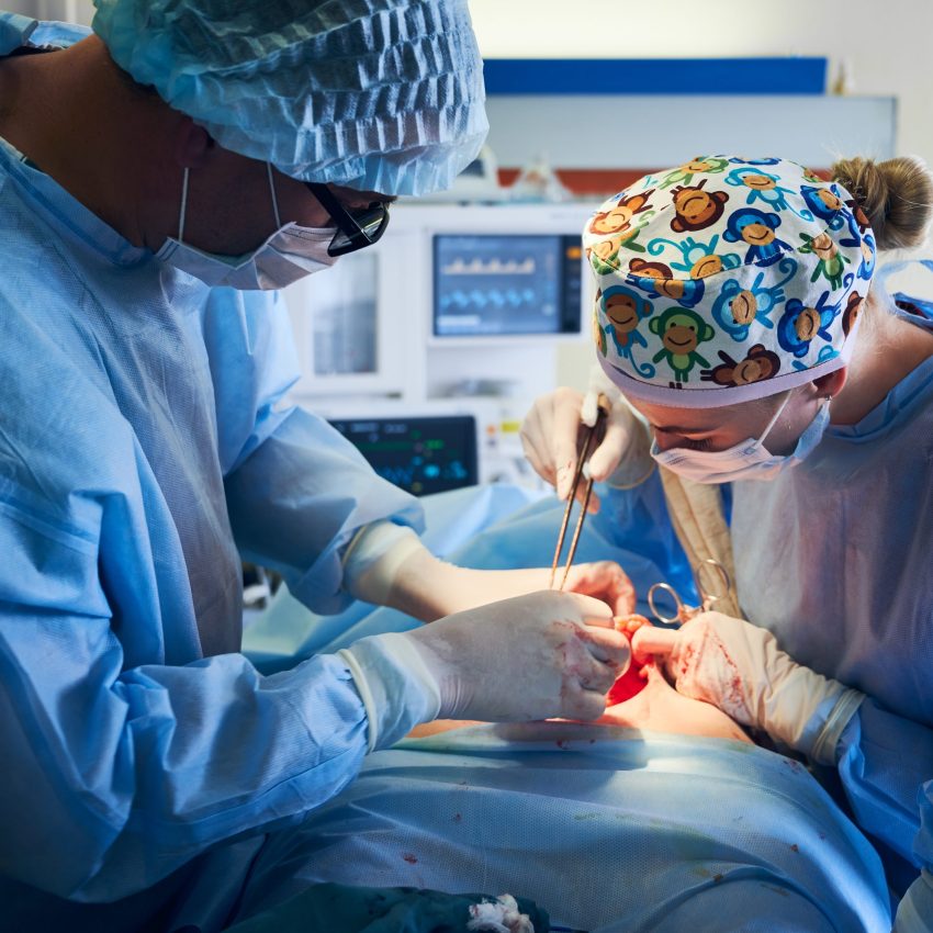 Close up of doctors performing plastical surgical operation in hospital. Surgeon and assistant using medical instruments and removing excess fat from patient abdomen. Concept of abdominoplasty.